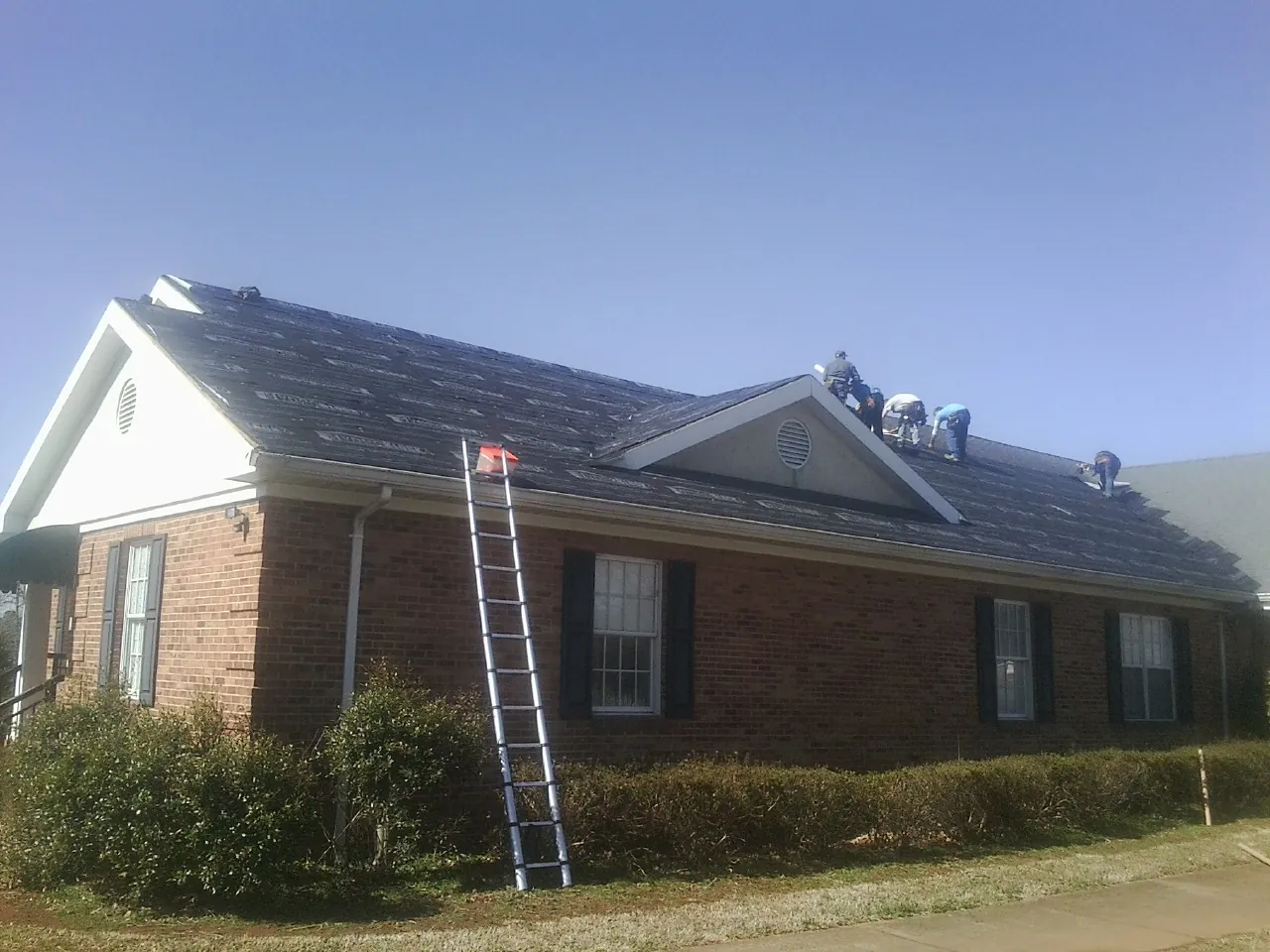 Crew tearing shingles off a brick ranch roof with a ladder set — Metal Roof Repair work by our crew in Meadville