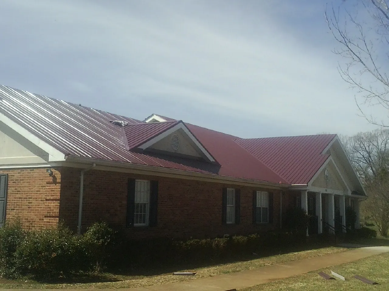 Red metal roof with gabled entries on a long brick building, from a Hail Damage Roof Repair job in Meadville