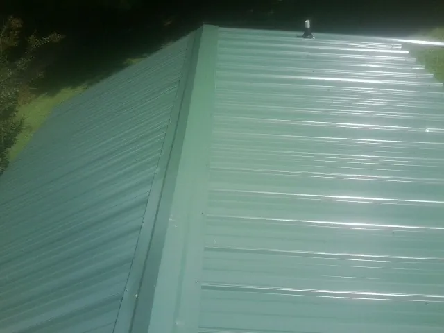 New green metal panels meeting at the ridge of a roof — Flat Roof Repair work by our crew in Meadville