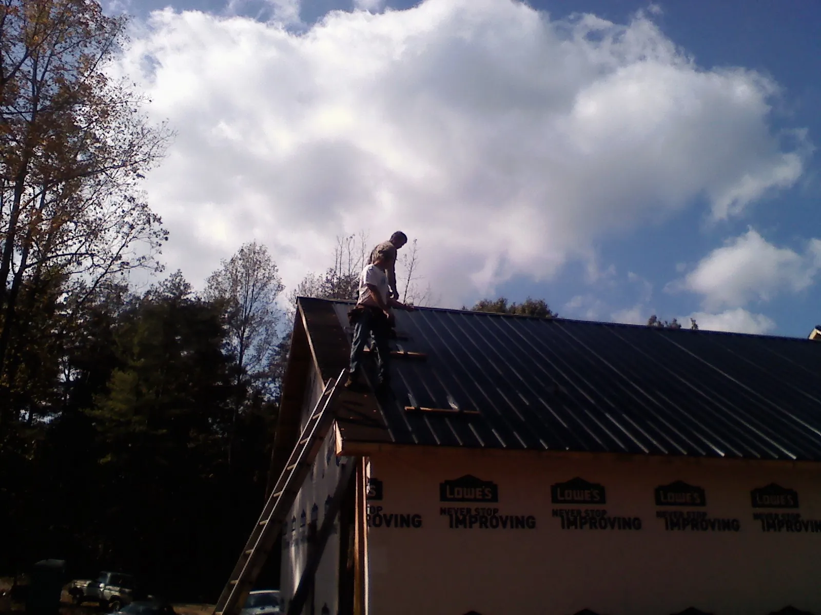 Roofer fastening dark metal panels high against a cloudy sky, from a Roof Inspection job in Meadville