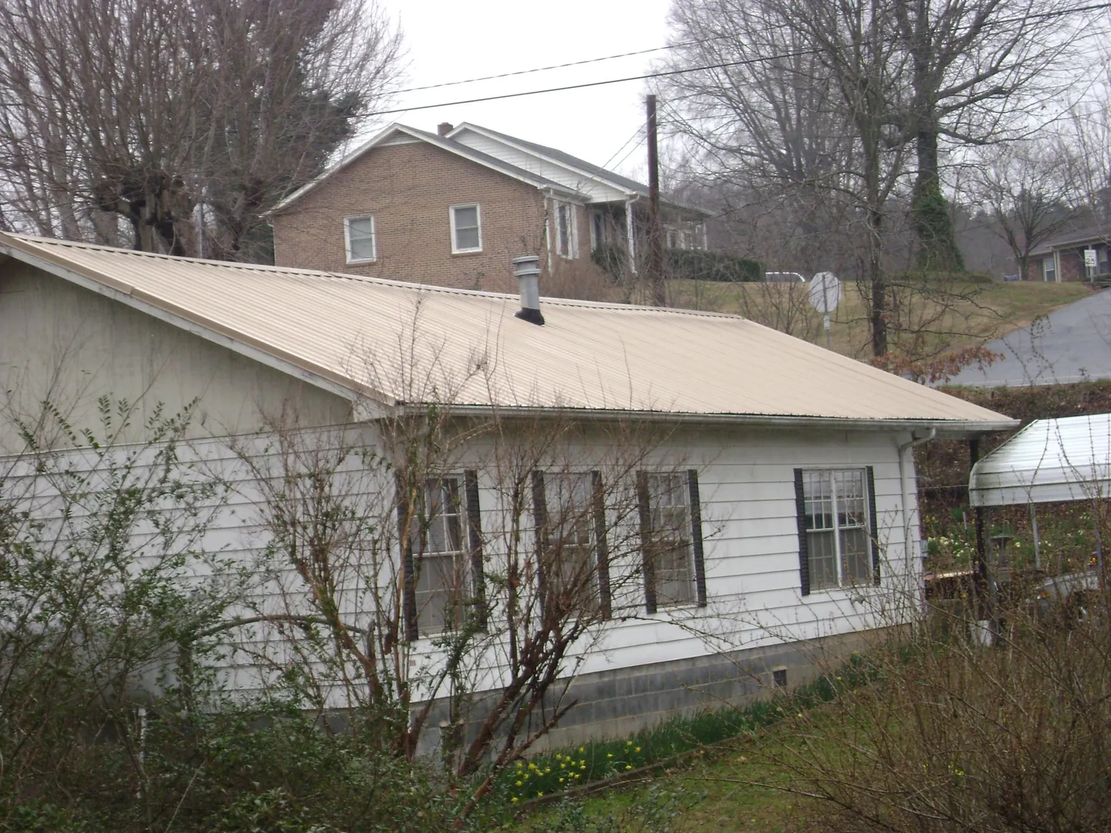 Tan metal roof on a white sided house set into a hillside — Commercial Roofing by Roofing Brothers in Meadville