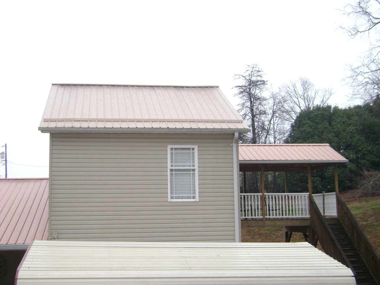 Tan metal roofs on a two story addition and attached porch, from a Roof Replacement job in Meadville